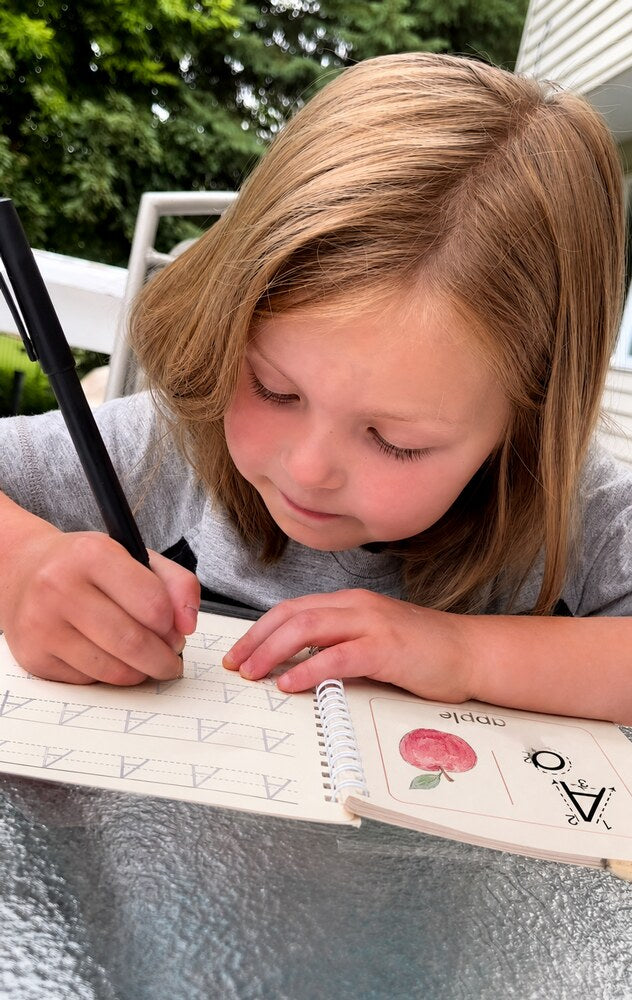 A girl traces the letter A in the Alphabet copybook