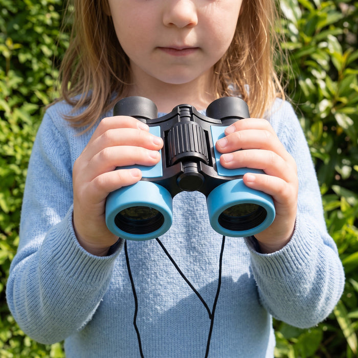 A child holds the binoculars in both hands in front of a hedge, showing they are about as wide as two small hands