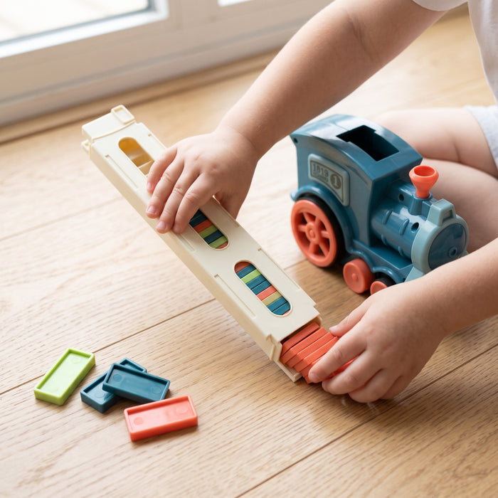 A child's hands slide orange dominoes into the end of the cream loading tower, with the train and loose dominoes nearby