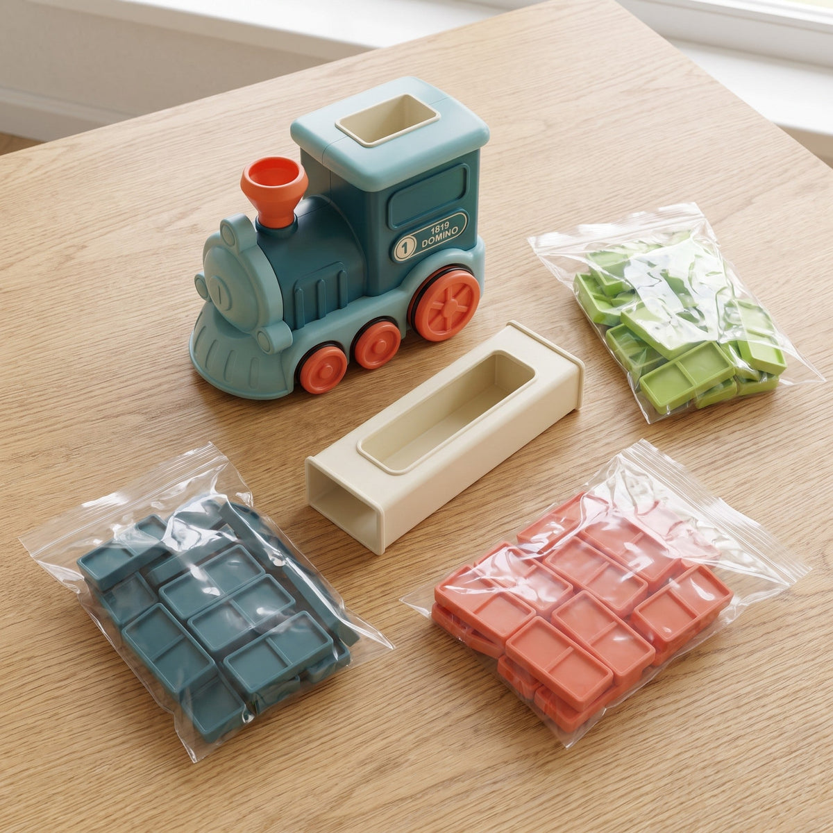 The set laid out: the train, the cream loading tower and three bags of dominoes in teal, green and orange