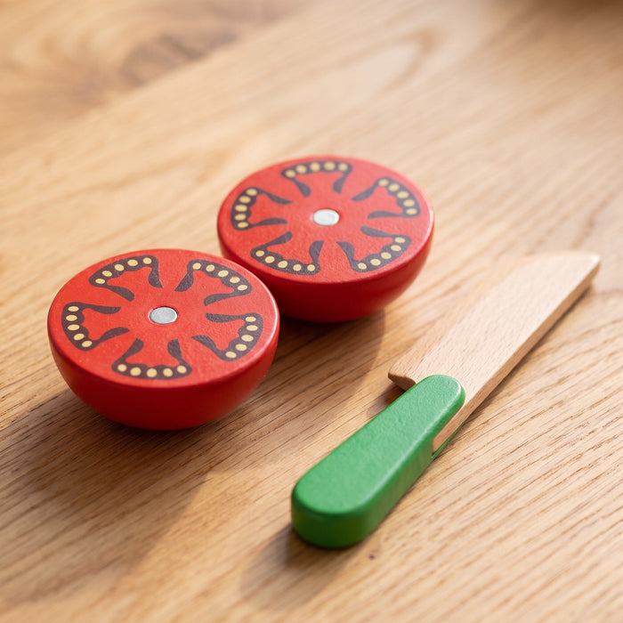 Close-up of two wooden tomato halves with a small metal disc in the middle of each cut side, beside a green-handled knife