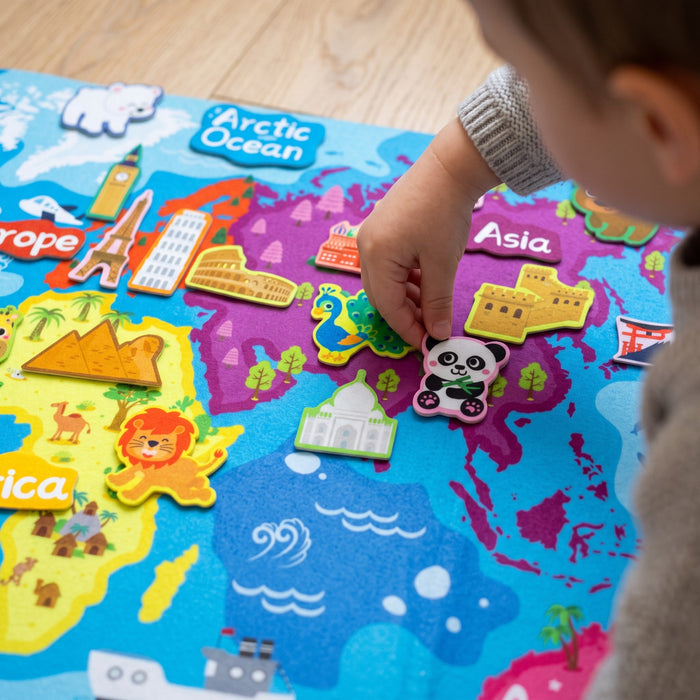 A child's hand presses a felt panda onto Asia, near felt pieces of the Great Wall, the Taj Mahal and a peacock