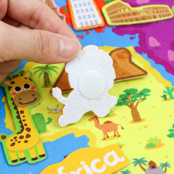 An adult's fingers turn the felt lion over to show the round hook-and-loop dot on its back, above Africa on the map