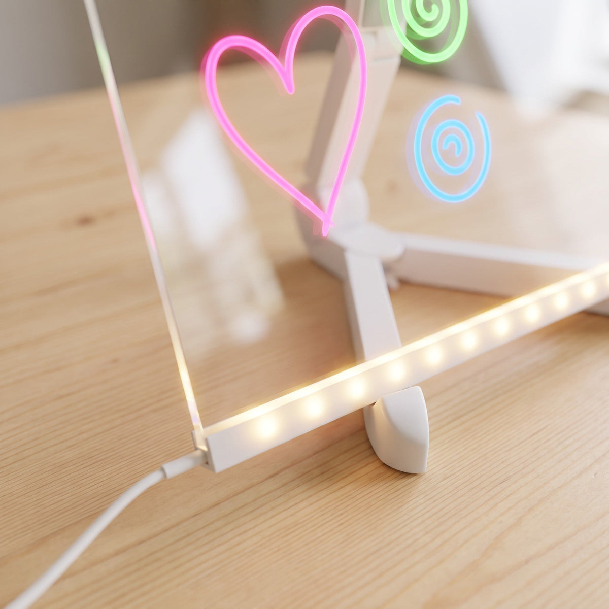 The glowing light bar along the bottom of the clear board up close, with the cable plugged in and a lit-up pink heart above.