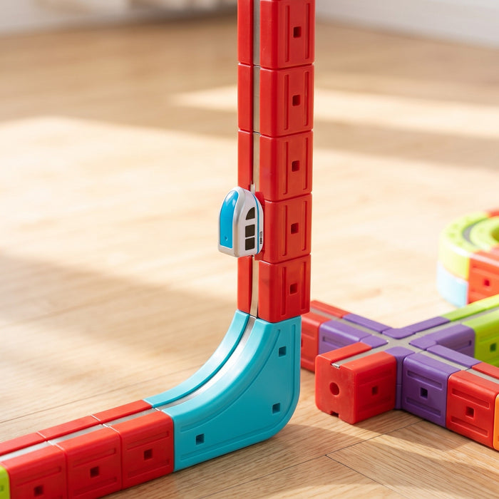 The small train climbs straight up a tall column of red track pieces, after a curved blue corner piece