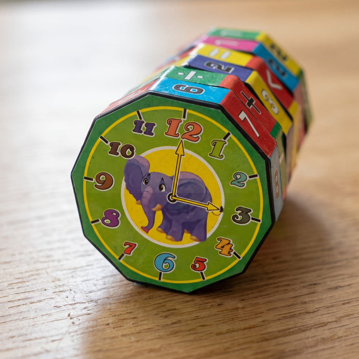 Close-up of the end of the tube: a clock face with the numbers 1 to 12, two yellow hands and a purple elephant
