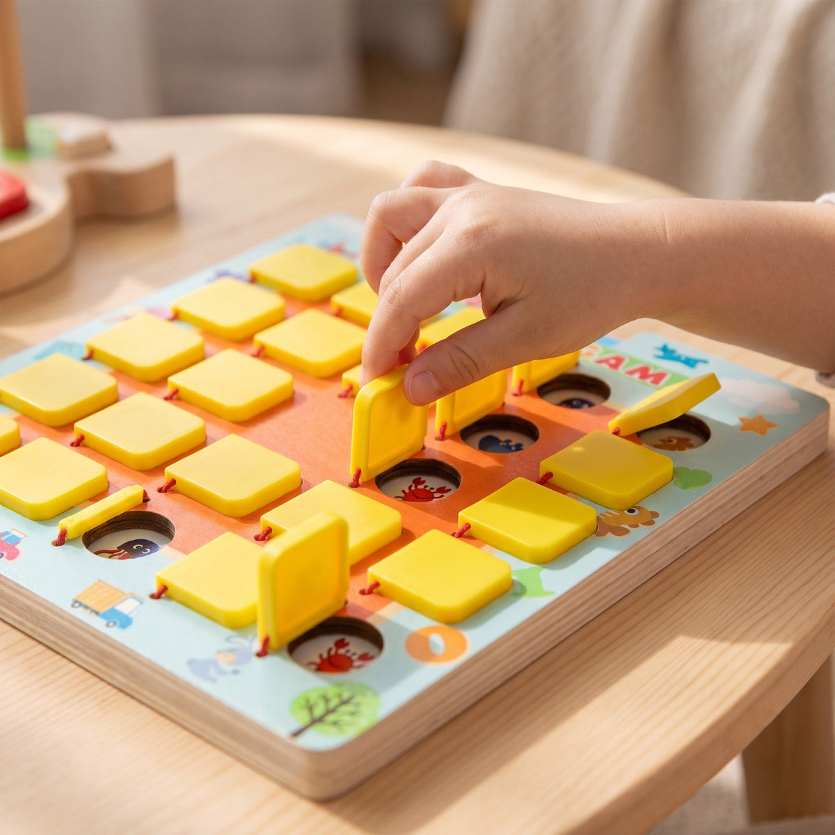 A child's hand lifts a yellow flap on the board to show a red crab picture underneath, with a few other flaps already open