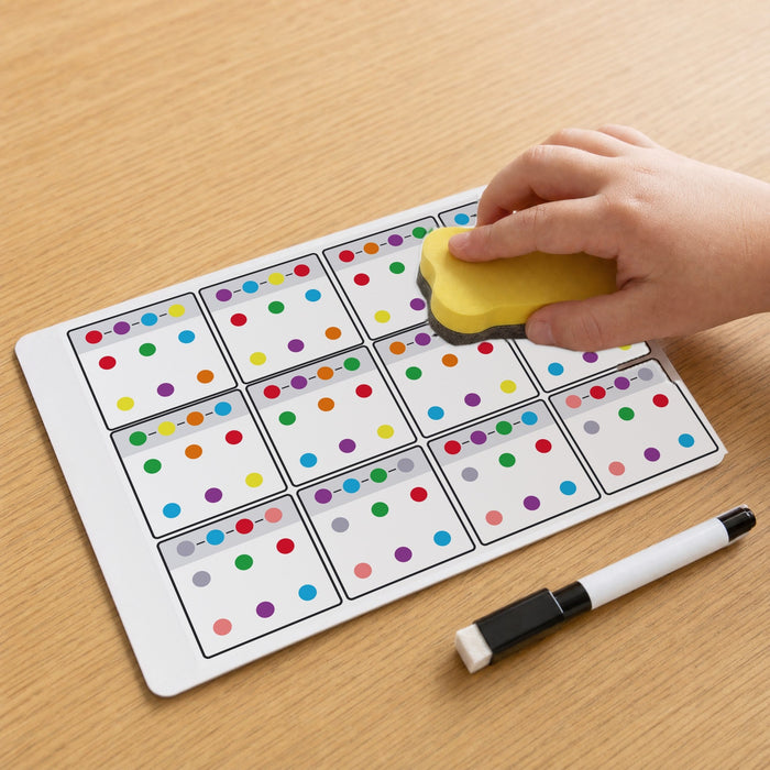 A child's hand wipes a puzzle card clean with the yellow eraser, with a black marker lying beside it.